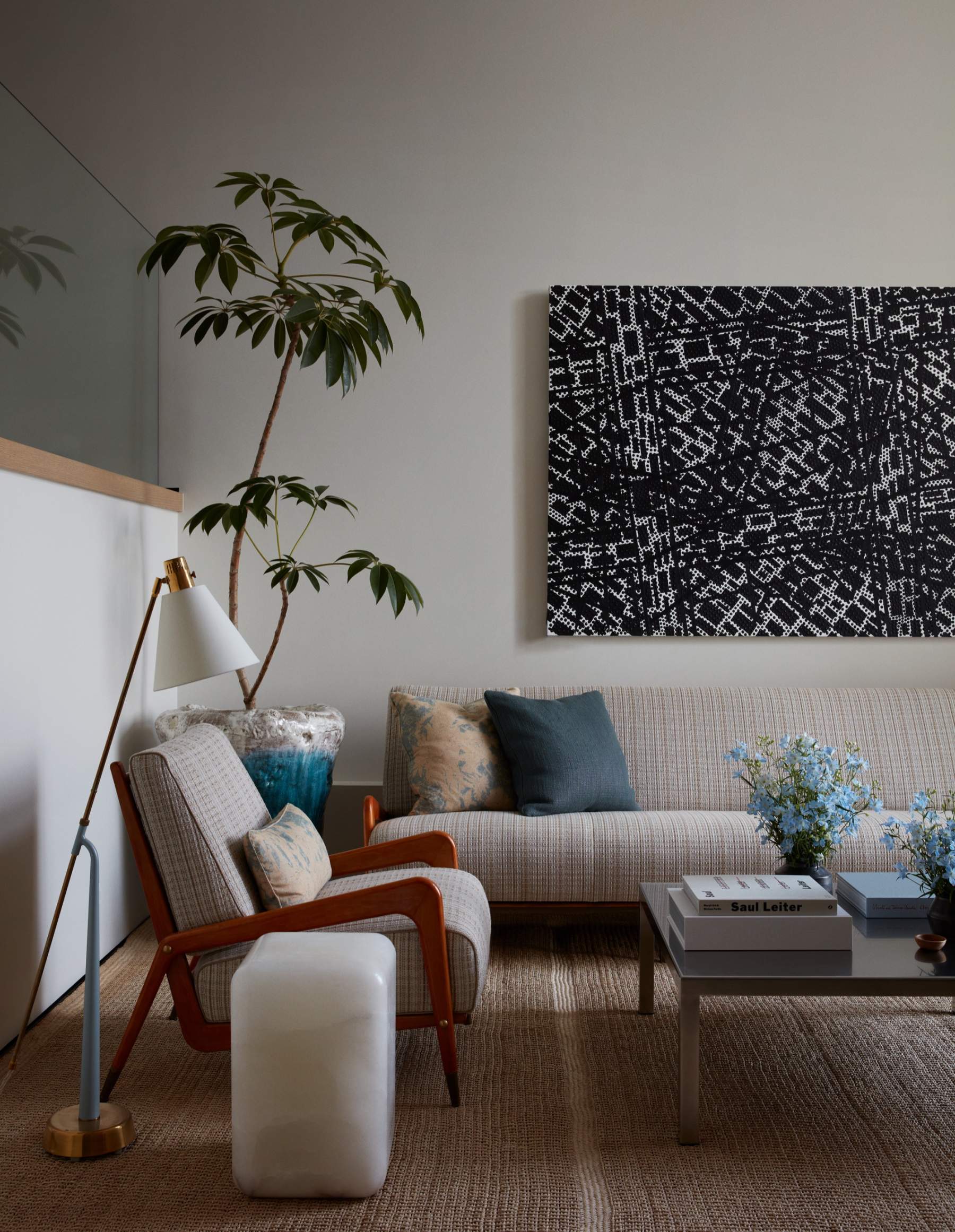 Living room with a woven rug, a tweed sofa, a wooden armchair and a large black-and-white painting